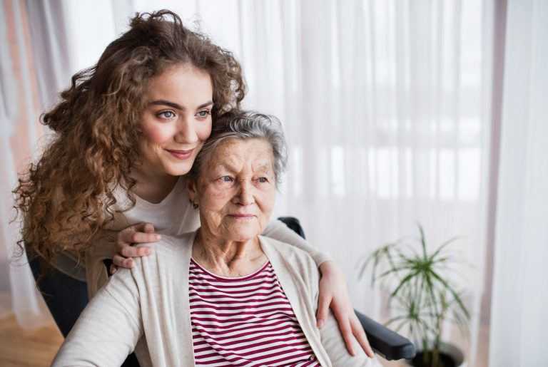 Mum & Daughter A young woman and an elderly woman share a thoughtful moment at a table with a notebook and cup.